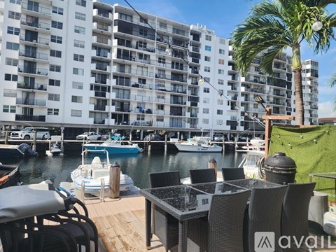 A white building with balconies is next to a body of water with boats docked.