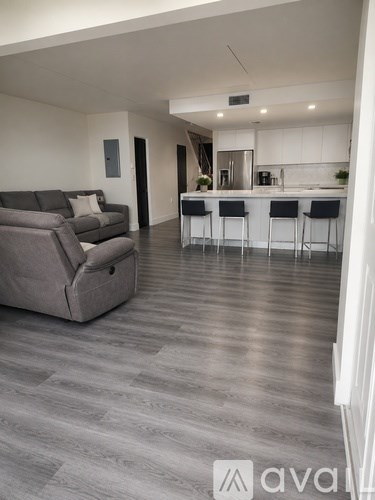 A modern living room with a grey sofa and a kitchen area in the background.