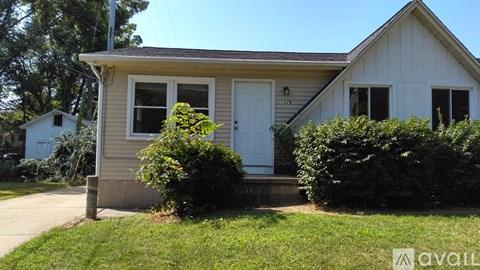 A house with a white door and windows surrounded by greenery.