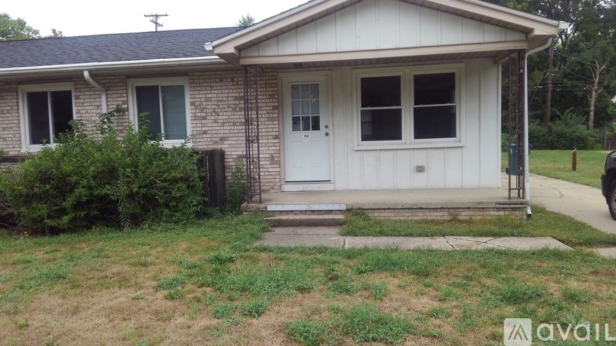 A small house with a white door and windows is surrounded by greenery.