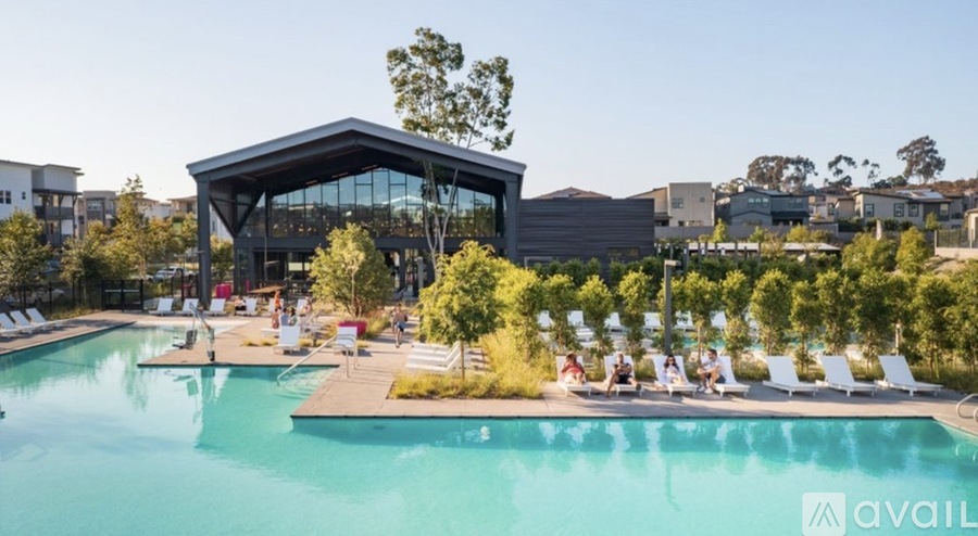 A large swimming pool with a building in the background and people relaxing by the poolside.