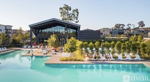 A large swimming pool with a building in the background and people relaxing by the poolside.