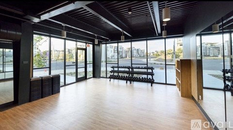 A spacious room with wooden floors and large windows overlooking a cityscape.