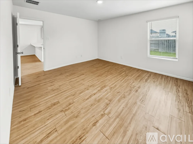 A room with wooden flooring and a window showing a building outside.
