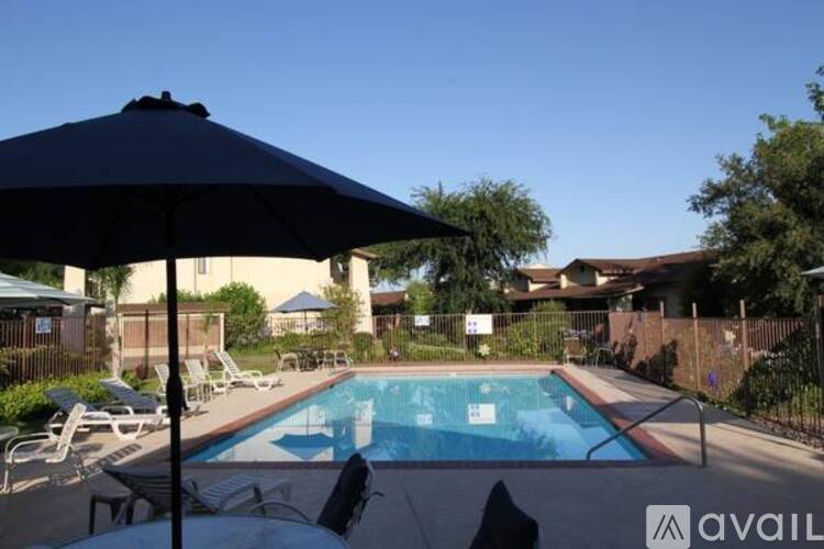 A pool with a black umbrella in the foreground and a house in the background.