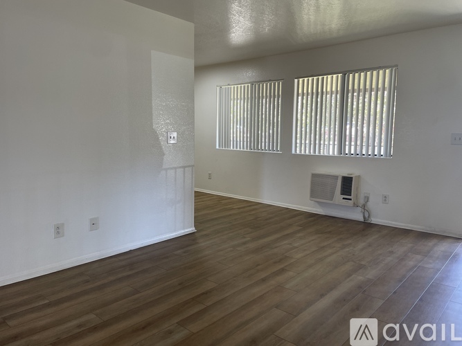 A spacious room with wooden flooring and a window with blinds.