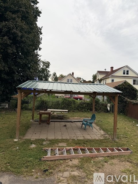 A wooden gazebo with a green roof is surrounded by a grassy area.