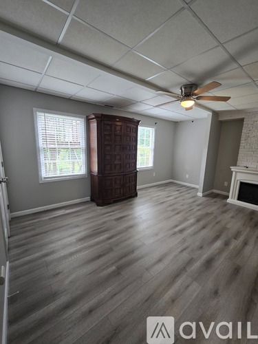 A room with a fan, wooden floor, and a fireplace.