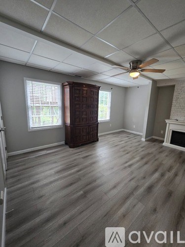 A room with a fan, wooden floor, and a fireplace.