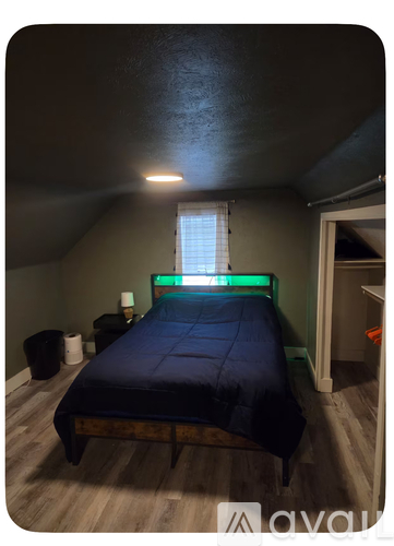 A bedroom with a bed, a window with blinds, a nightstand, and a trash can.