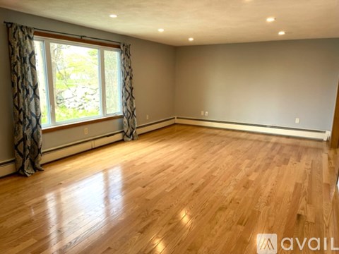 A room with wooden flooring and a window with curtains.
