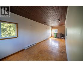 A room with a wooden ceiling and floor, a window, and a green trash can.