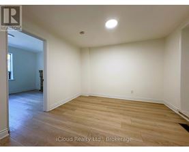 A room with wooden flooring and white walls, with a doorway leading to another room.