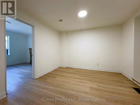 A room with wooden flooring and white walls, with a doorway leading to another room.