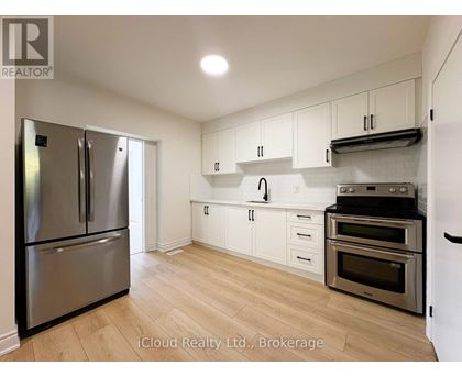 A kitchen with a stainless steel refrigerator and oven, white cabinets, and wooden flooring.