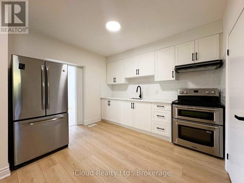 A kitchen with a stainless steel refrigerator and oven, white cabinets, and wooden flooring.