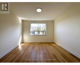 A room with wooden flooring and a window showing a view of trees.