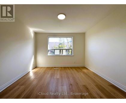 A room with wooden flooring and a window showing a view of trees.