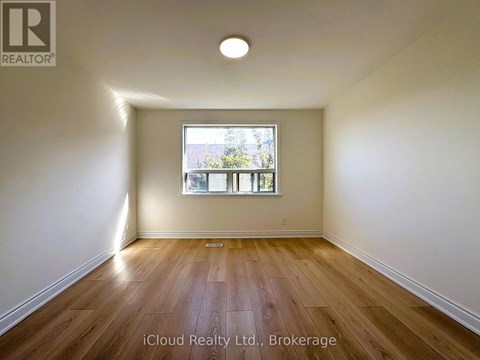 A room with wooden flooring and a window showing a view of trees.