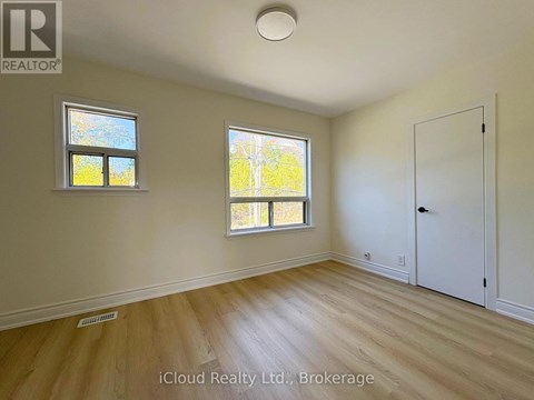 A room with wooden flooring and two windows.