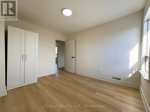 A room with wooden floors and white walls, with a door on the right and two white doors on the left.