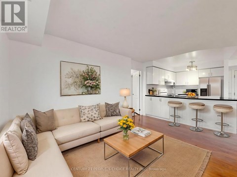 A living room with a beige couch, a coffee table, and a kitchen area in the background.