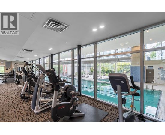 A gym with a row of treadmills and a swimming pool in the background.