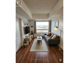 A living room with a grey couch, a wooden floor, and a large window.