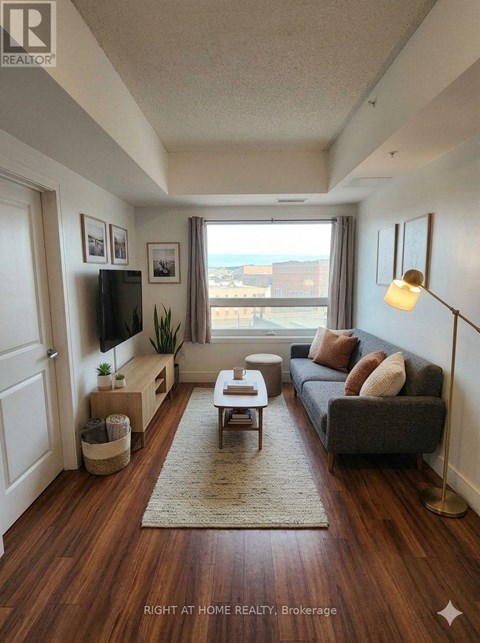 A living room with a grey couch, a wooden floor, and a large window.