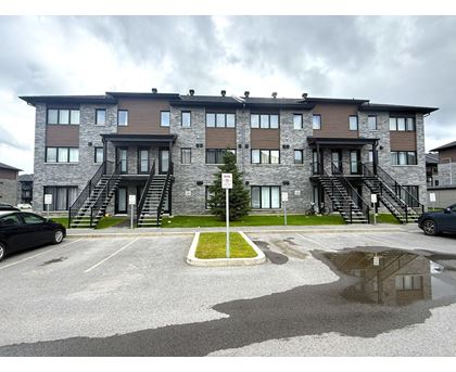 A large building with a grey and brown exterior and a small green area in front.