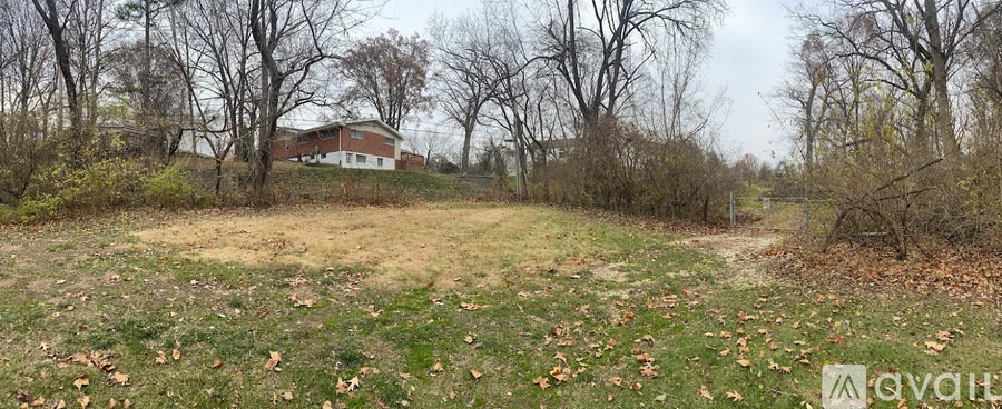 A grassy field with trees and a house in the background.
