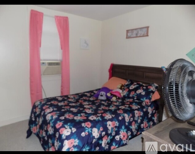 A bed with a floral comforter and a fan on a table.