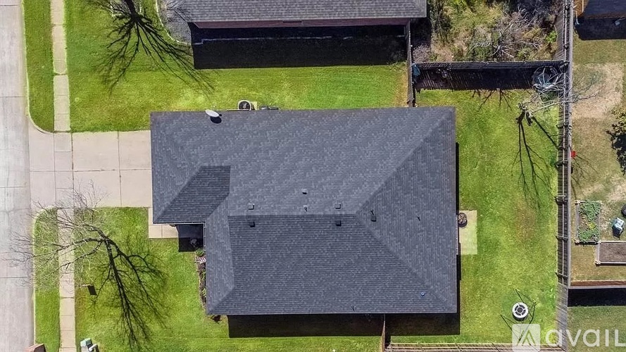 A large grey building with a black roof is surrounded by a grassy area.