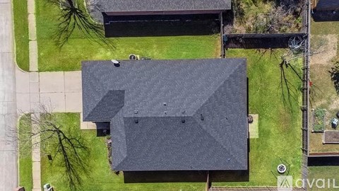 A large grey building with a black roof is surrounded by a grassy area.