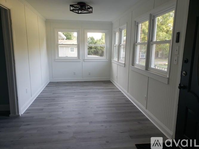 A room with white walls and wooden flooring, with a window on the right side.