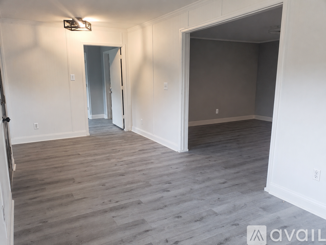 A room with a wooden floor and white walls, with a doorway leading to another room.