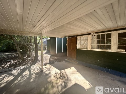 A sunlit covered walkway leads to a building with a brown door.