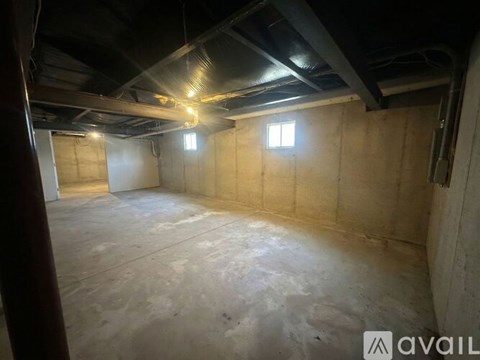 A spacious attic room with exposed beams and two windows.