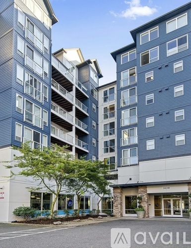 A modern apartment building with a blue and white exterior and a tree in front.