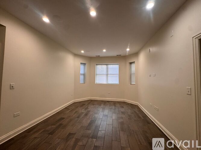 A spacious room with wooden flooring and two windows.
