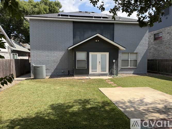 A house with a grey facade and a white door is surrounded by a green lawn.