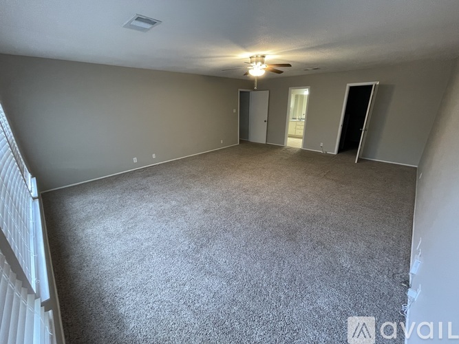 A spacious room with grey carpeting and a ceiling fan.