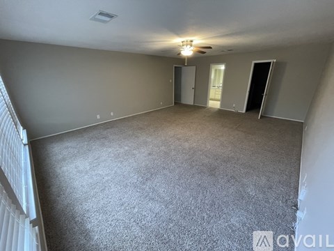 A spacious room with grey carpeting and a ceiling fan.