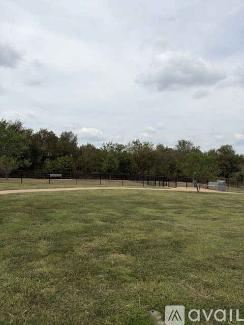 A grassy field with trees and a fence in the distance.