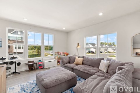 A living room with a grey sofa and a large window overlooking a street.
