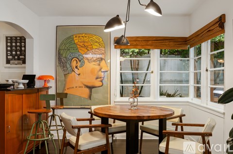 A dining room with a table and chairs and a painting of a head on the wall.