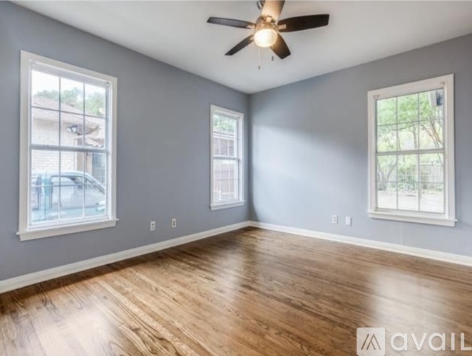 A spacious room with a ceiling fan and hardwood flooring.