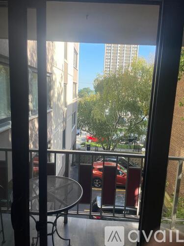 A balcony with a table and chairs overlooks a parking lot and buildings.