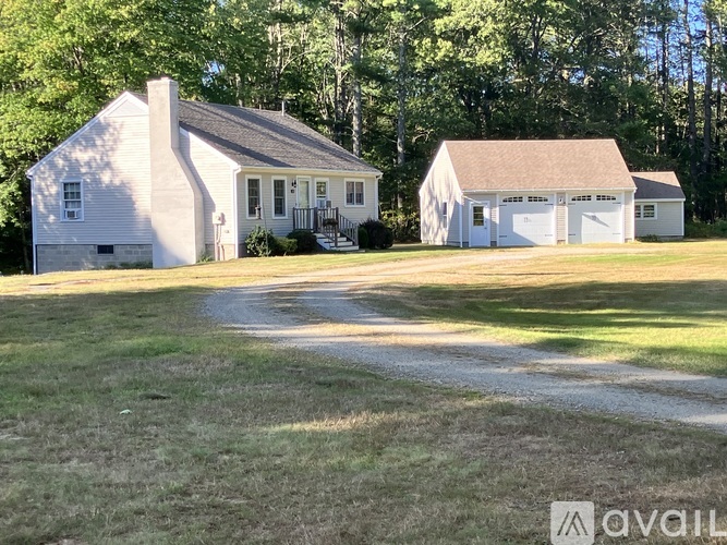 A white house with a garage is surrounded by green grass and trees.
