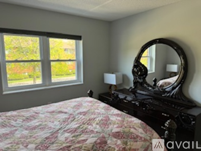 A bedroom with a bed, dresser, mirror, and window.